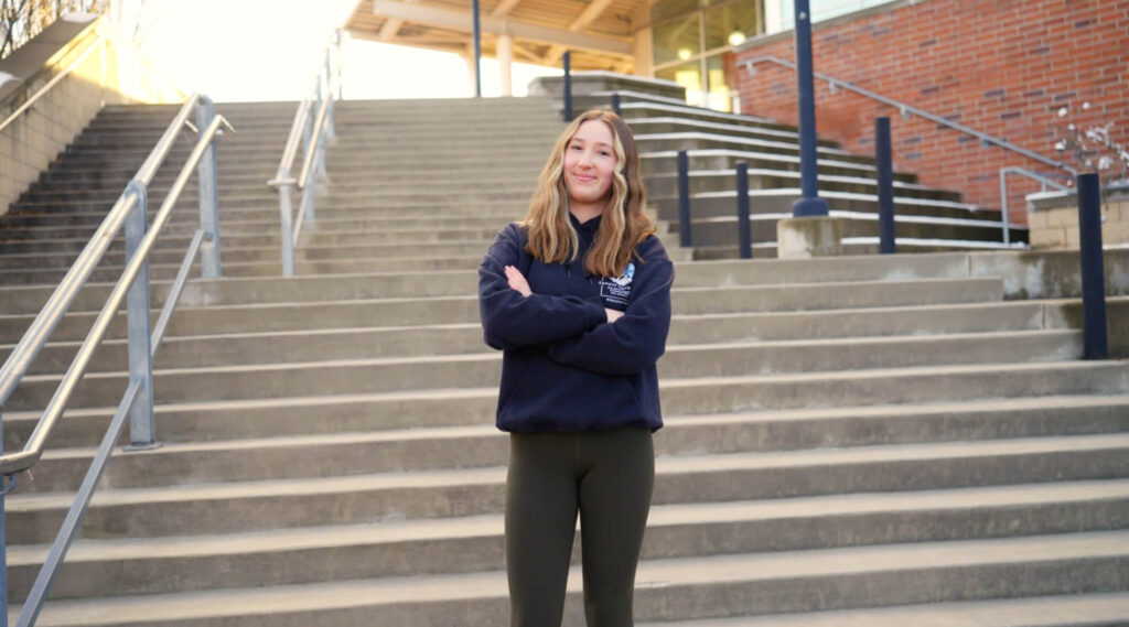 Woman stands on stairs with arms crossed.